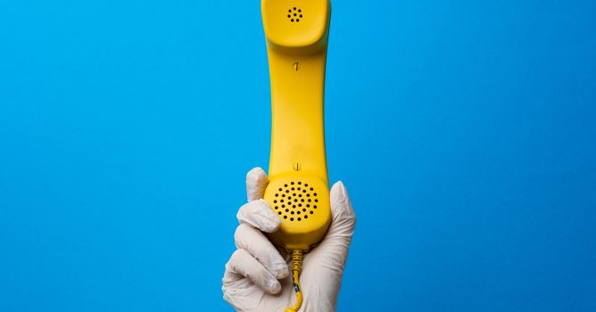 Female hand in medical glove holding yellow telephone speaker